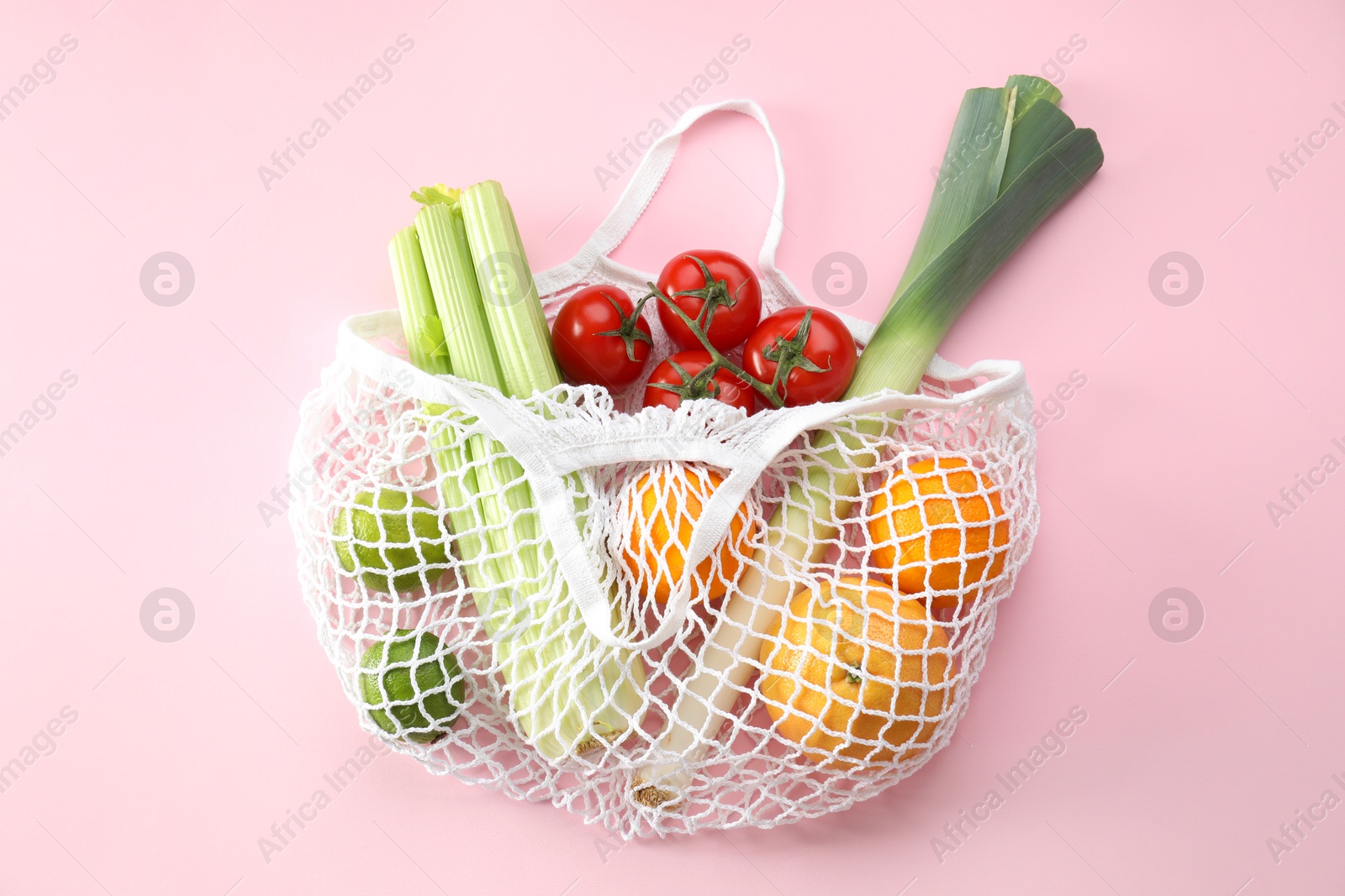 Photo of String bag with different vegetables and fruits on pink background, top view