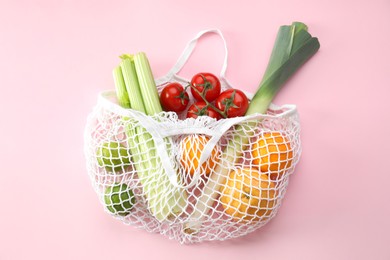 String bag with different vegetables and fruits on pink background, top view