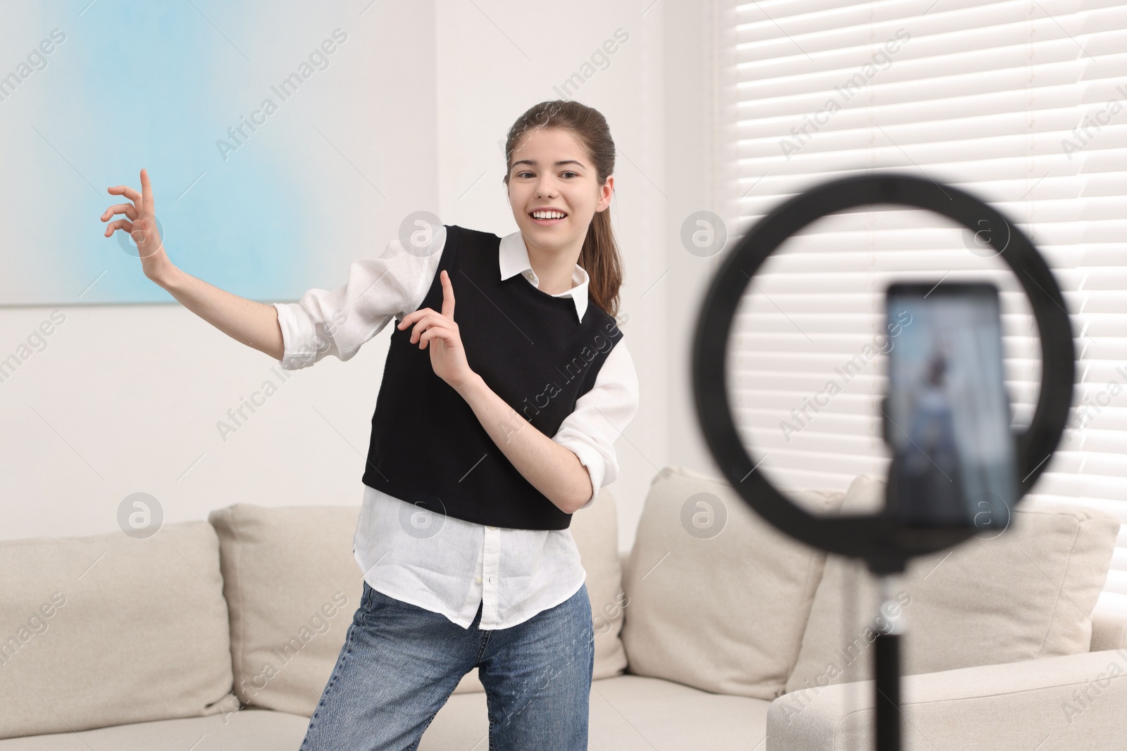 Photo of Smiling teenage blogger dancing while streaming at home