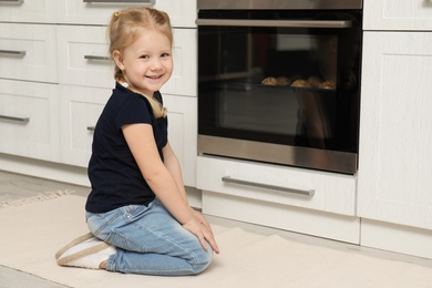 Little girl waiting for preparation of cookies in oven at home