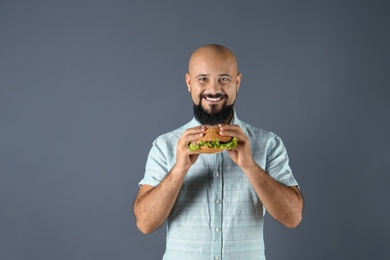 Overweight man with hamburger on gray background