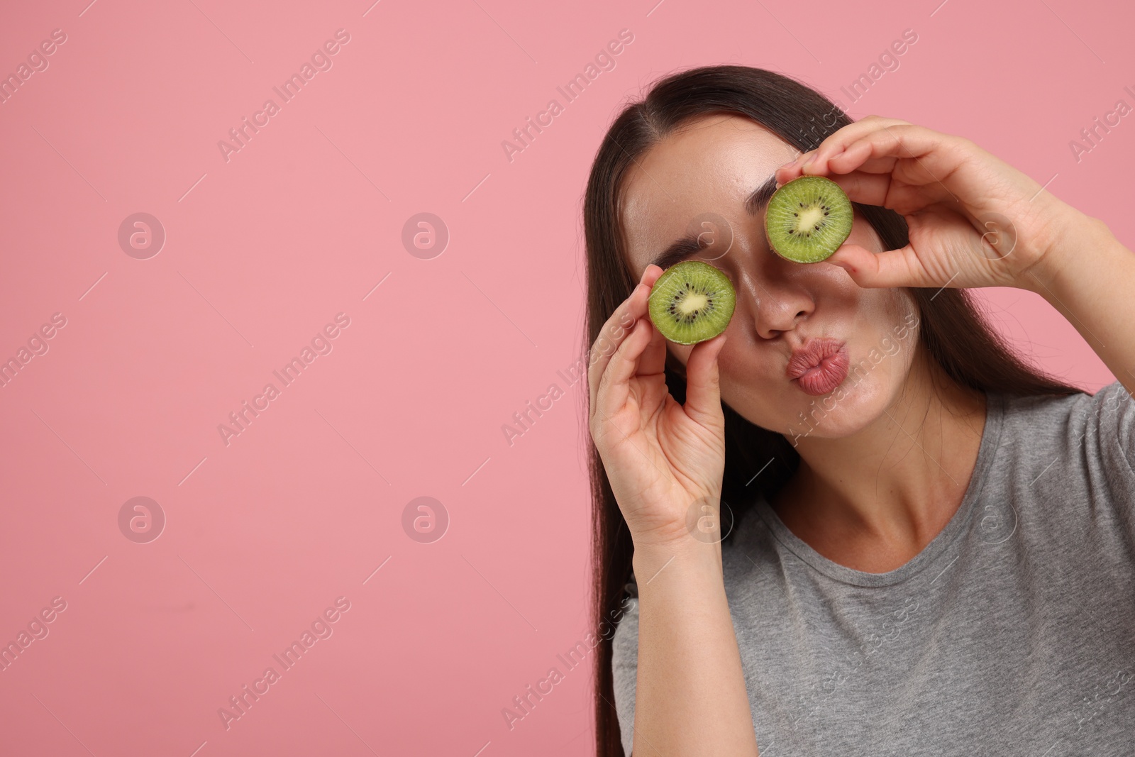 Photo of Woman covering eyes with halves of kiwi on pink background, space for text