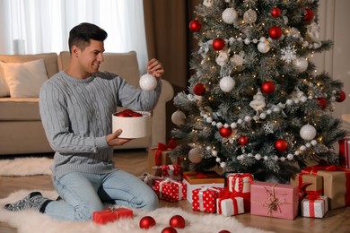 Photo of Handsome man decorating Christmas tree at home