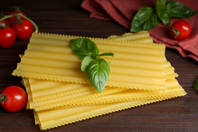 Photo of Uncooked lasagna sheets with cherry tomatoes and basil on wooden table