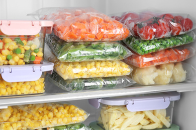 Plastic bags and containers with different frozen vegetables in refrigerator