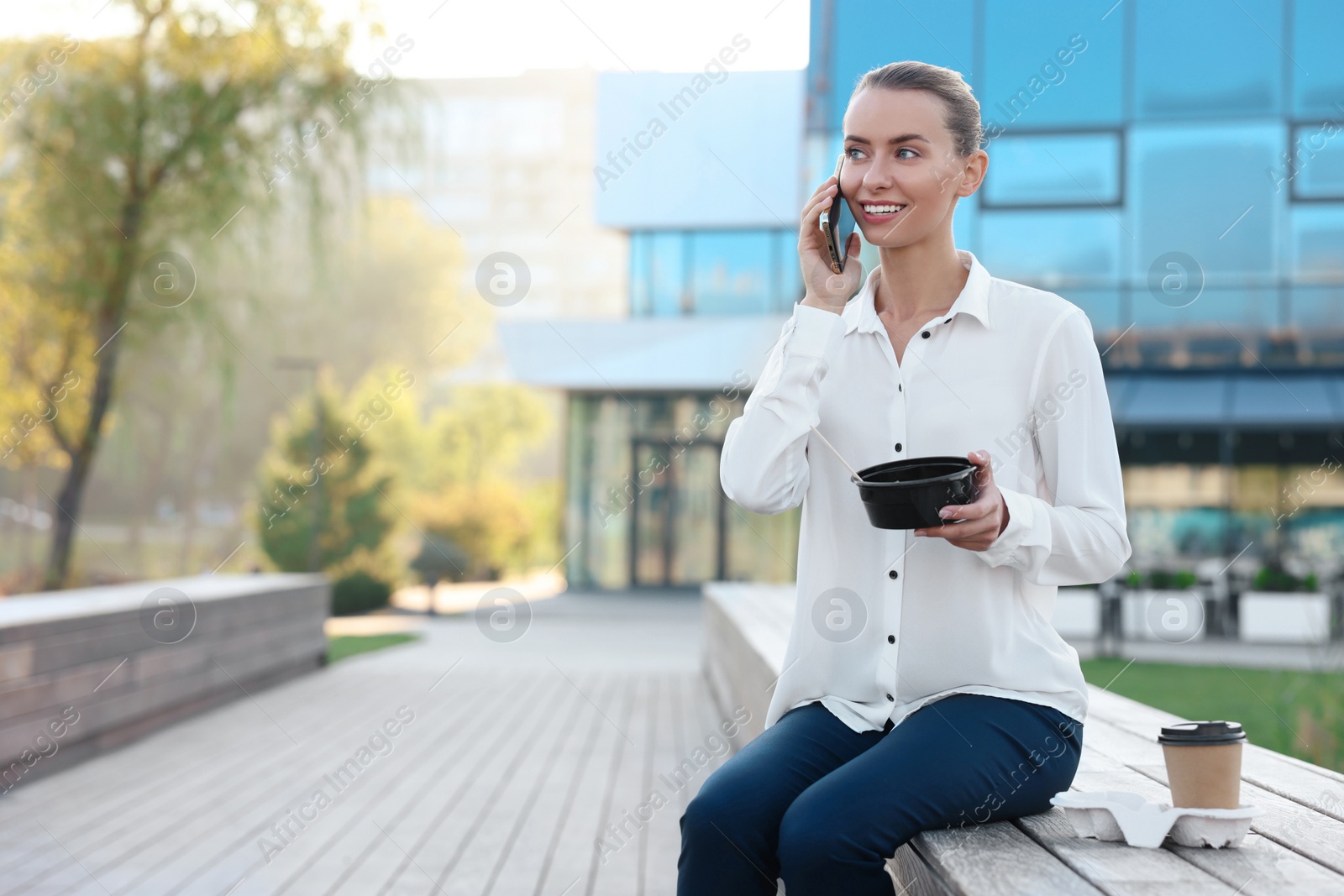 Photo of Smiling businesswoman talking on smartphone during lunch outdoors. Space for text