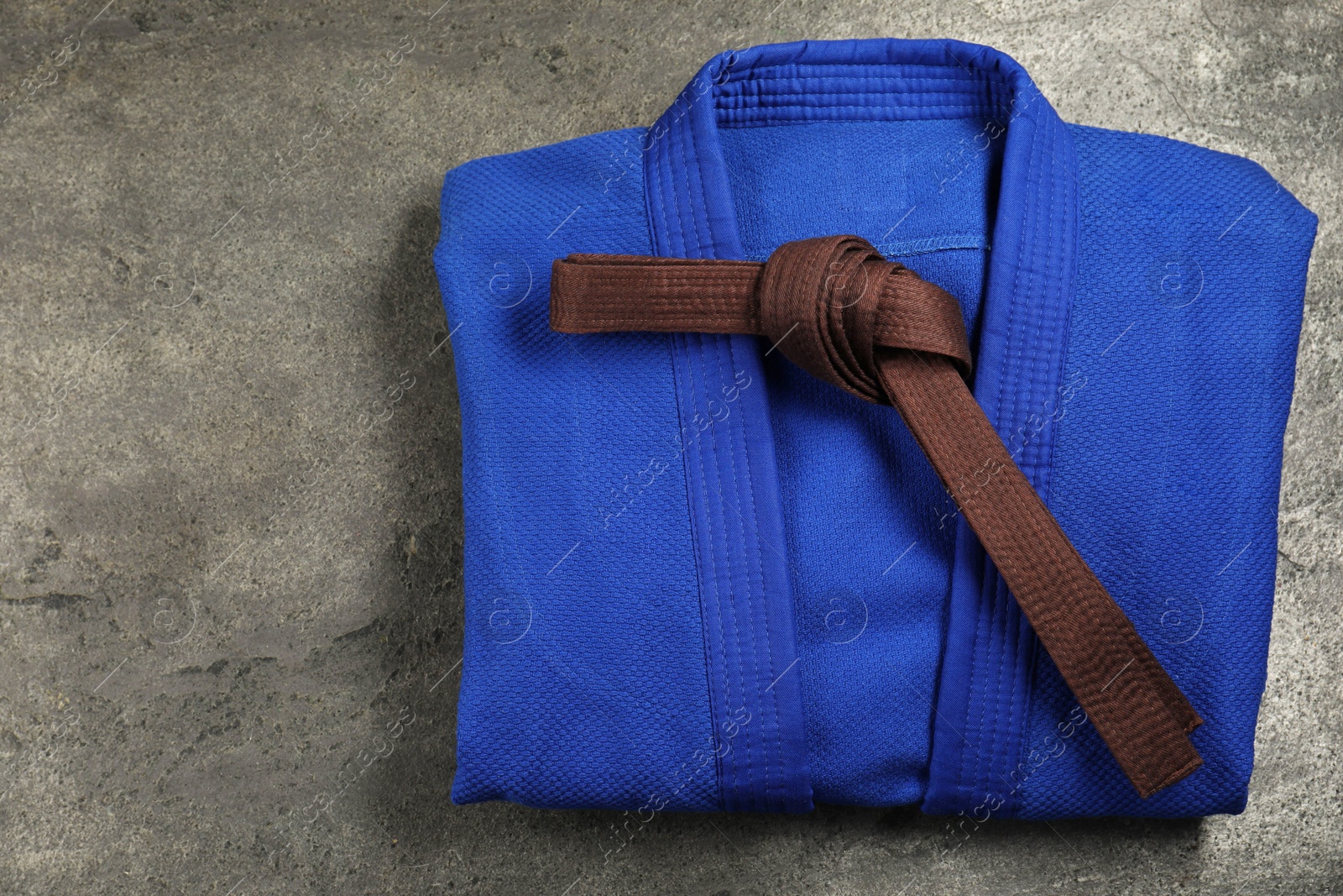 Photo of Brown karate belt and blue kimono on gray textured background, top view. Space for text