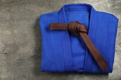 Brown karate belt and blue kimono on gray textured background, top view. Space for text