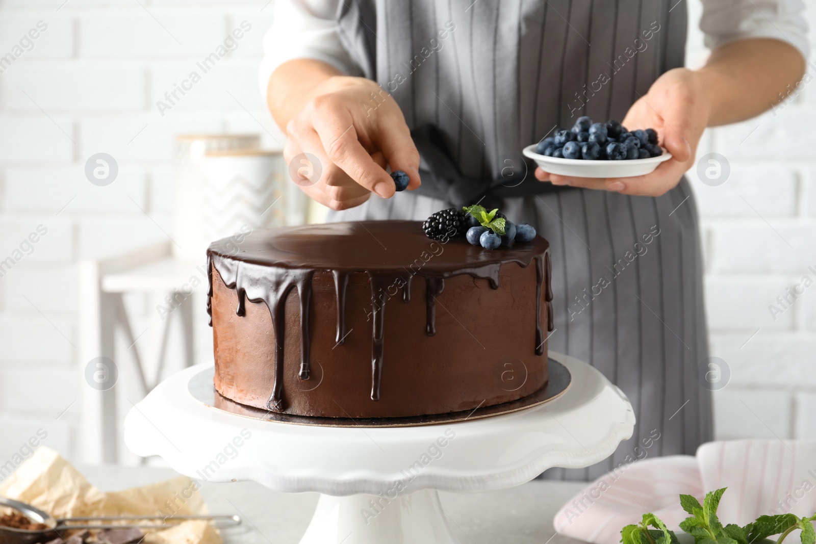 Photo of Baker decorating fresh delicious homemade chocolate cake with berries on table, closeup