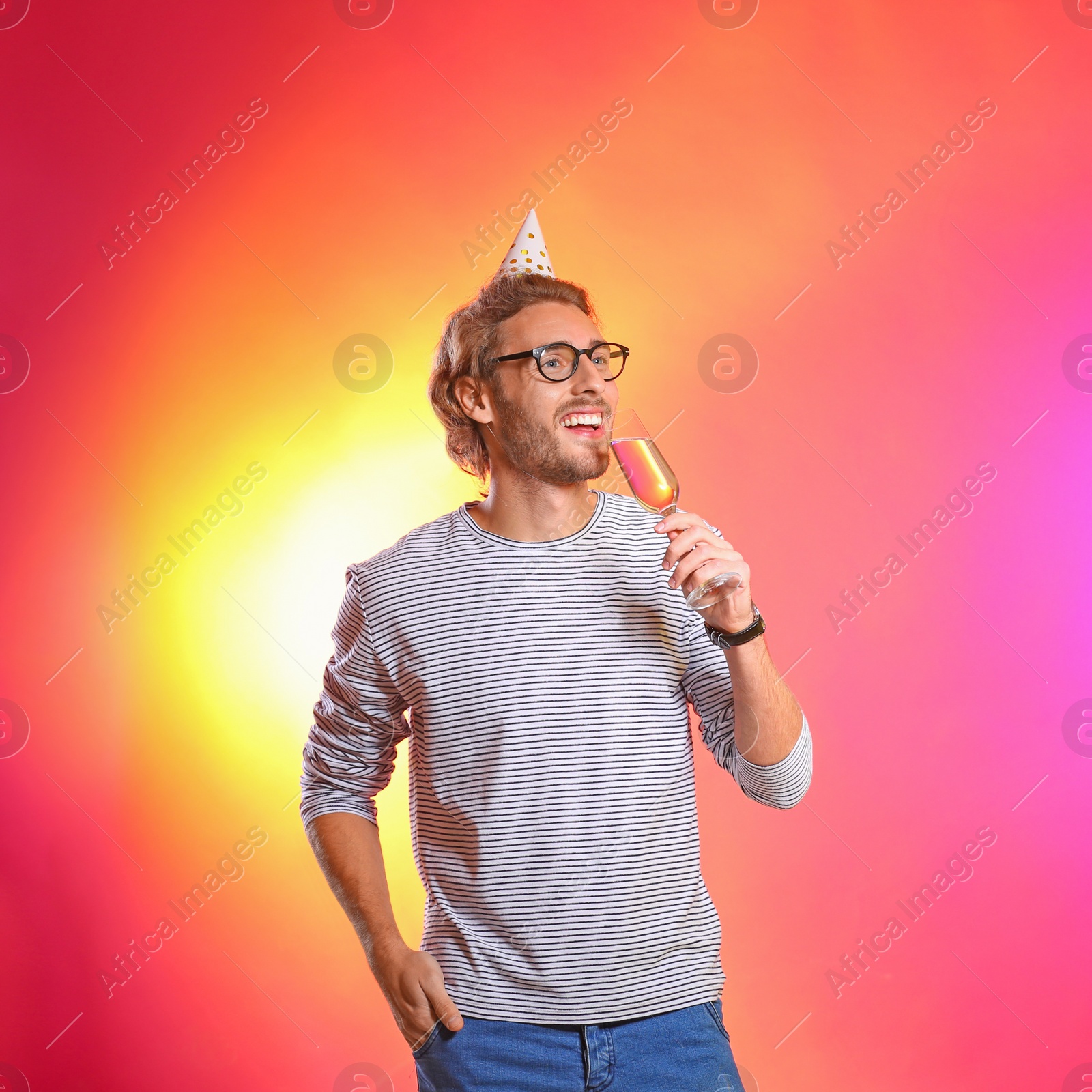 Photo of Portrait of happy man with party cap and champagne in glass on color background