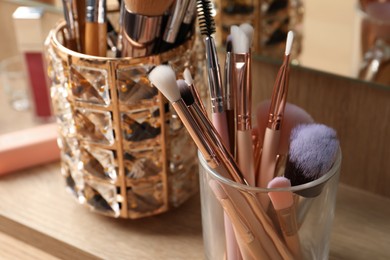 Set of professional brushes and makeup products near mirror on wooden table, closeup