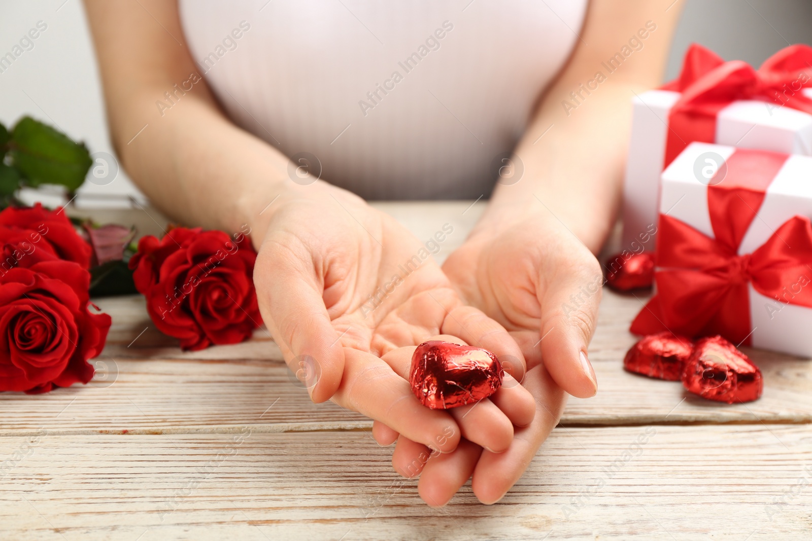 Photo of Woman holding heart shaped chocolate candy at white wooden table, closeup