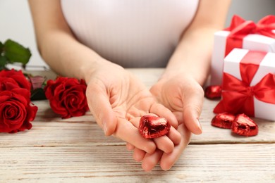 Woman holding heart shaped chocolate candy at white wooden table, closeup