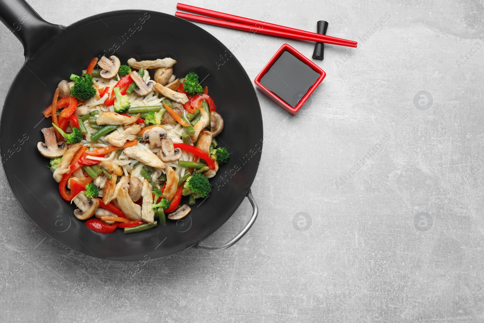 Photo of Stir fried noodles with mushrooms, chicken and vegetables in wok on light grey table, flat lay. Space for text