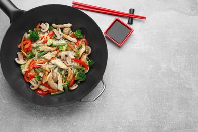 Photo of Stir fried noodles with mushrooms, chicken and vegetables in wok on light grey table, flat lay. Space for text