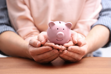 Couple with piggy bank at wooden table, closeup