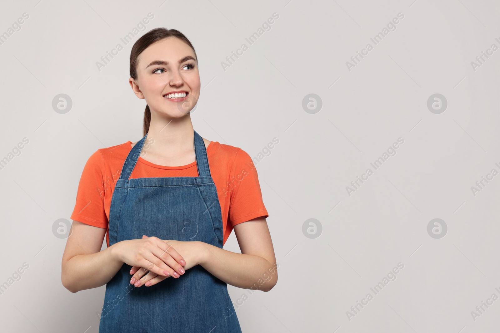 Photo of Beautiful young woman in clean denim apron on light grey background. Space for text
