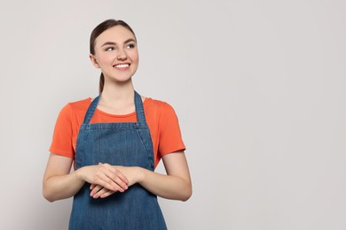 Photo of Beautiful young woman in clean denim apron on light grey background. Space for text