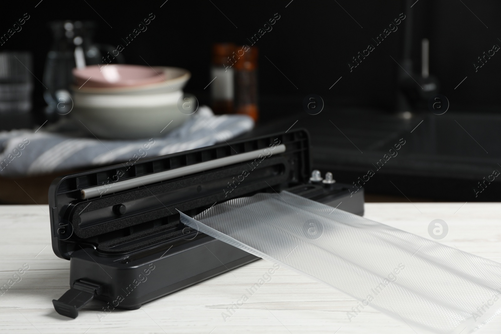 Photo of Sealer for vacuum packing with plastic bag on white wooden table in kitchen