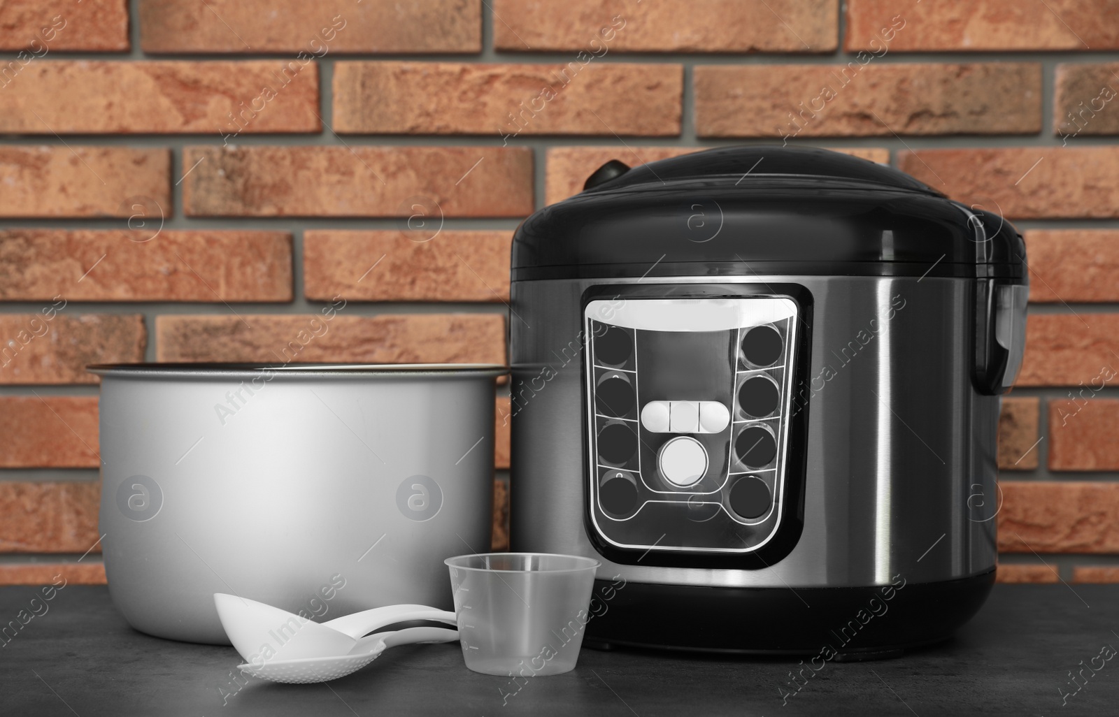 Photo of Modern electric multi cooker, parts and accessories on table near brick wall