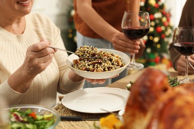 Photo of Woman with bowl of traditional Christmas kutia and her family at festive dinner, closeup. Slavic dish