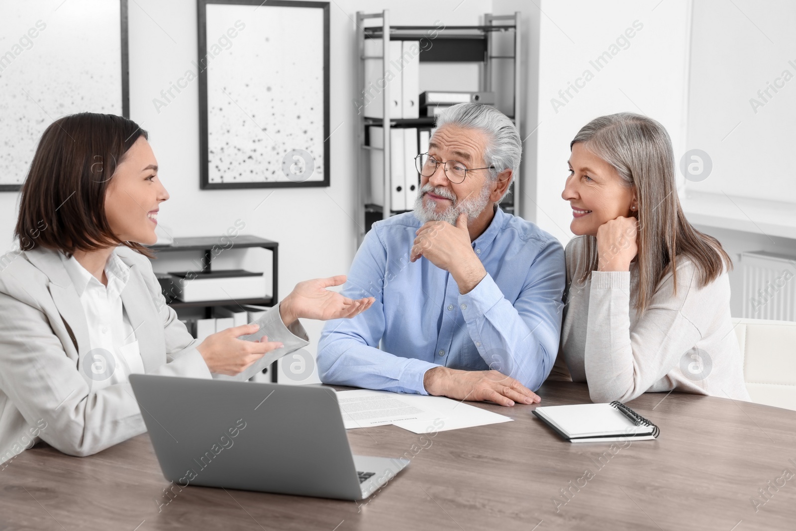 Photo of Elderly couple consulting insurance agent about pension plan at wooden table indoors