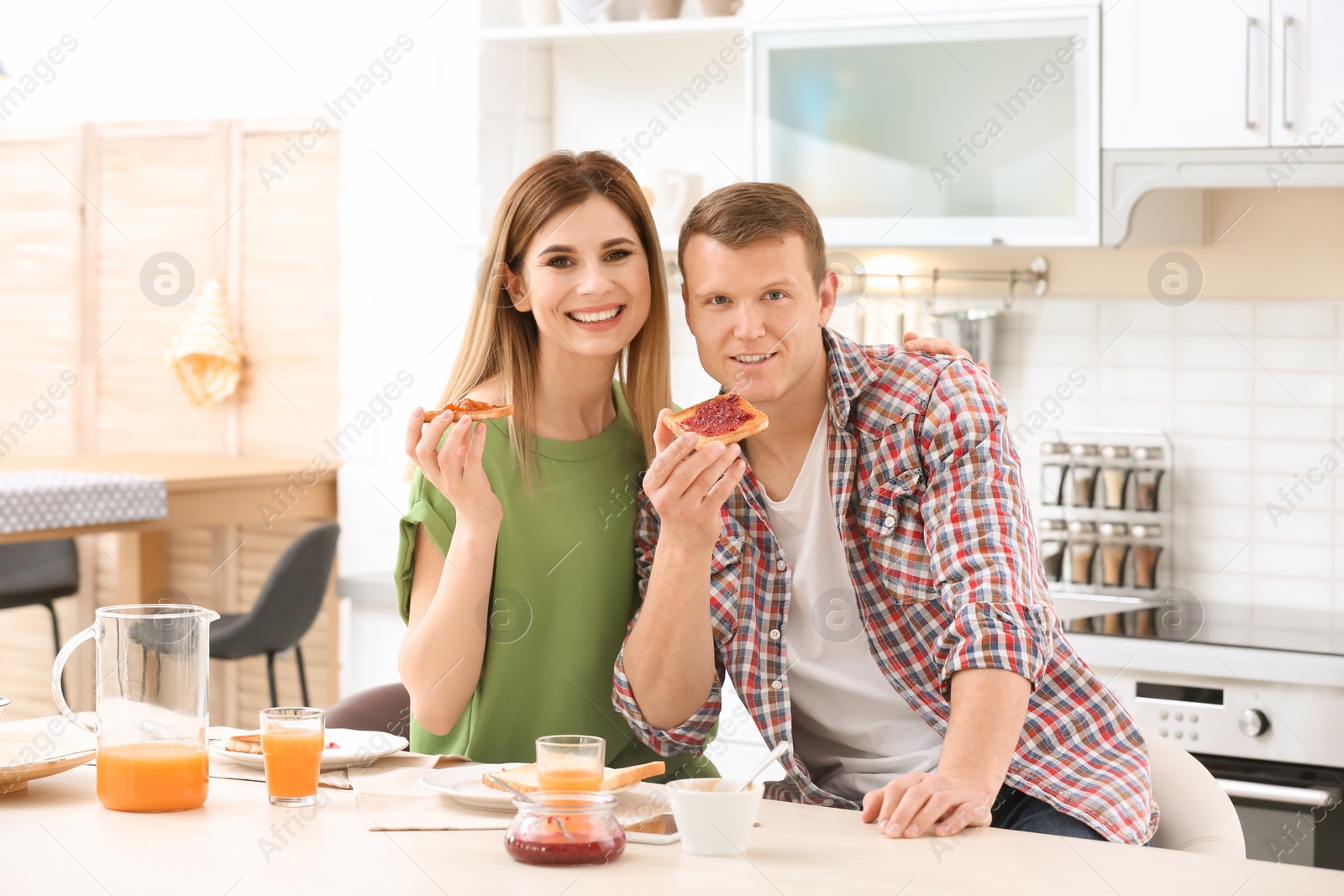 Photo of Happy lovely couple having breakfast with tasty toasted bread at table in kitchen