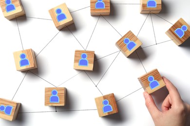 Image of Teamwork. Woman arranging wooden cubes with human icons linked together symbolizing cooperation at white table, top view