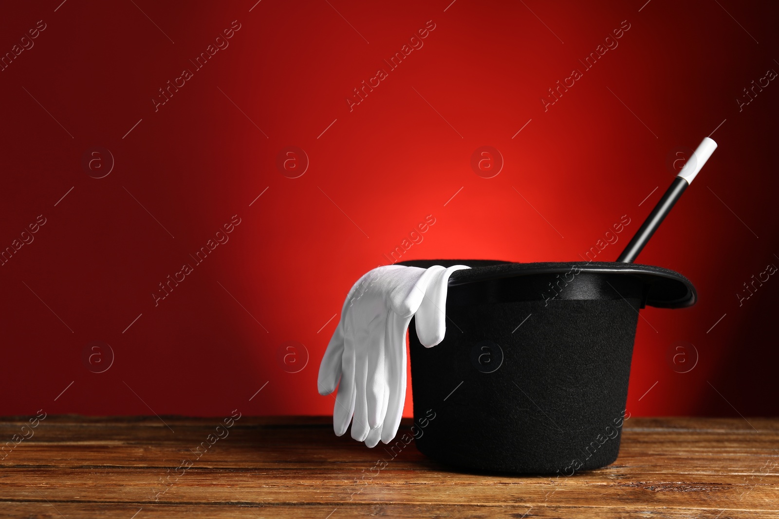 Photo of Magician's hat, gloves and wand on wooden table against red background, space for text