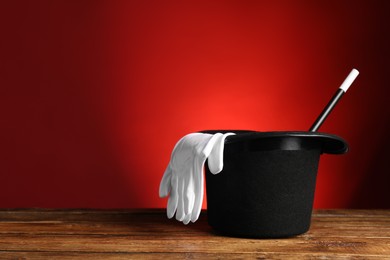 Photo of Magician's hat, gloves and wand on wooden table against red background, space for text