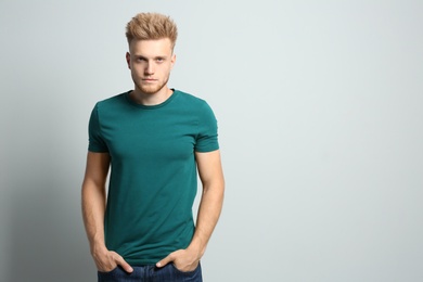 Young man wearing blank t-shirt on light background. Mockup for design