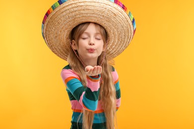 Photo of Cute girl in Mexican sombrero hat blowing kiss on orange background