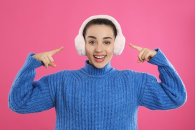 Photo of Beautiful young woman wearing earmuffs on pink background