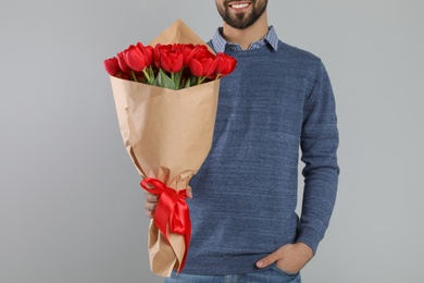 Happy man with red tulip bouquet on light grey background, closeup. 8th of March celebration