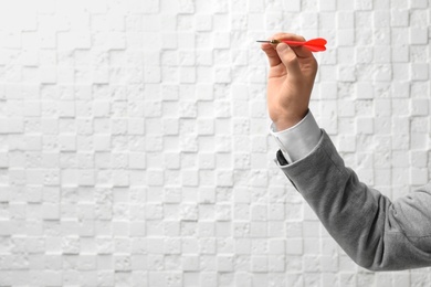 Man holding dart against light wall. Business trainer concept