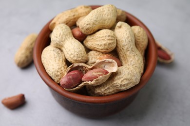 Fresh unpeeled peanuts in bowl on grey table, closeup