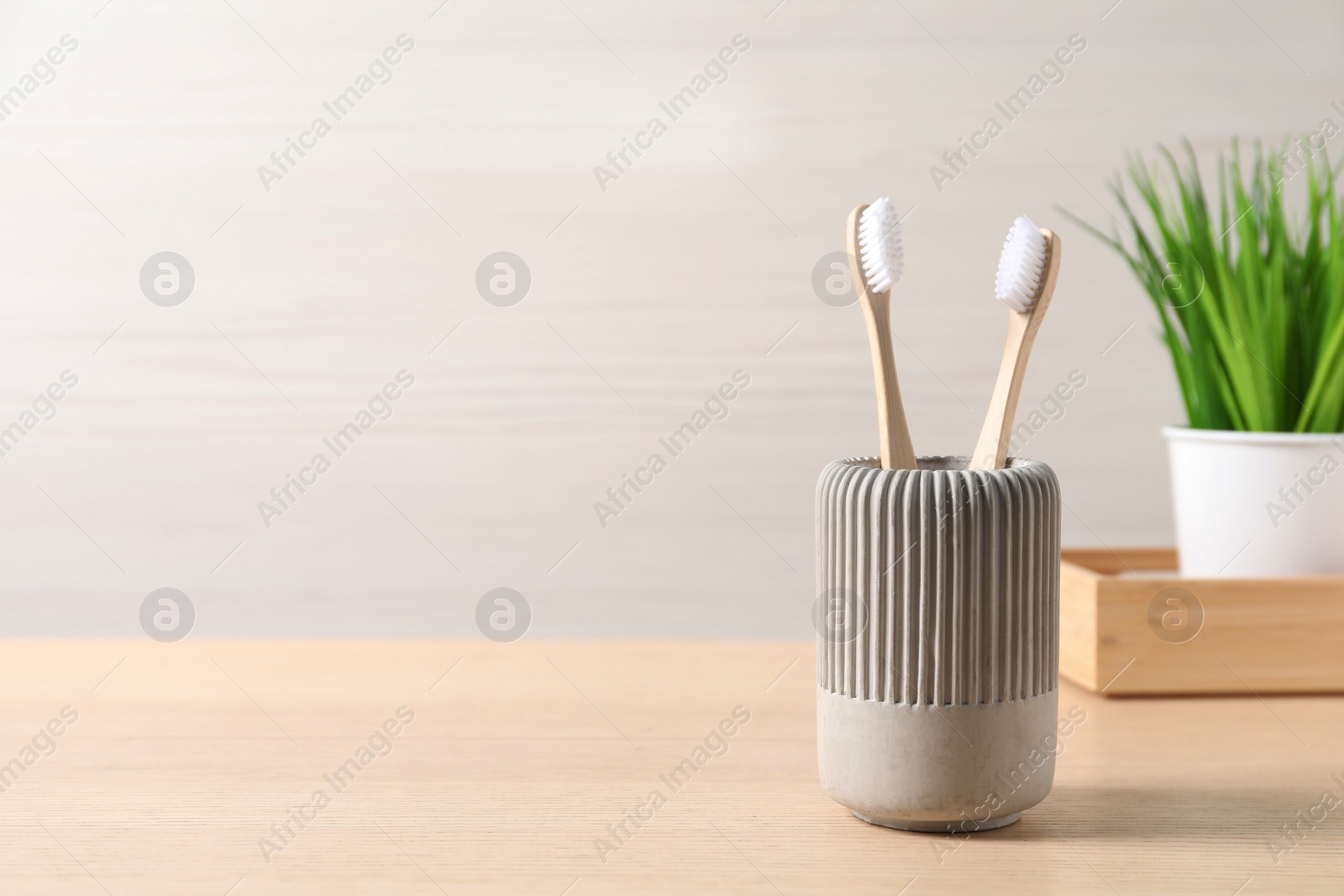 Photo of Bamboo toothbrushes in holder on wooden table, space for text