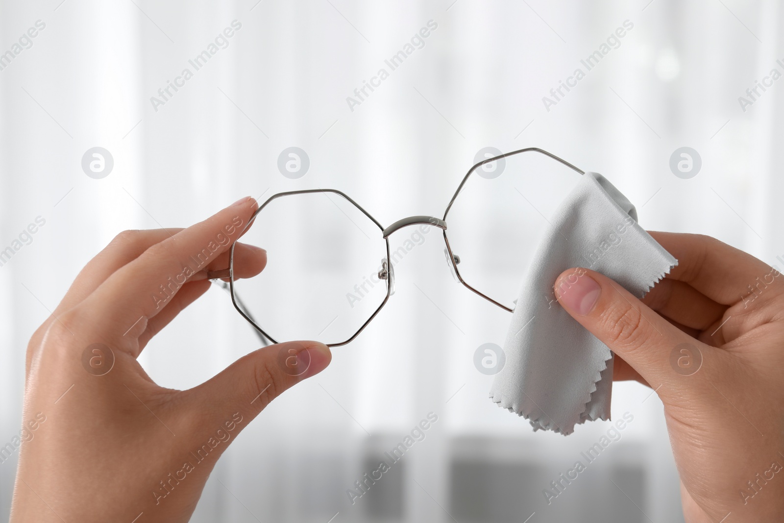 Photo of Woman wiping her glasses with microfiber cloth at home, closeup