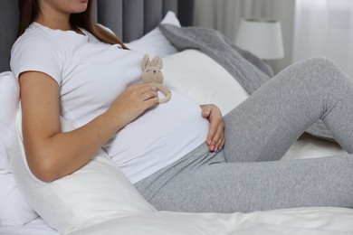 Photo of Pregnant woman with bunny toy in bedroom, closeup