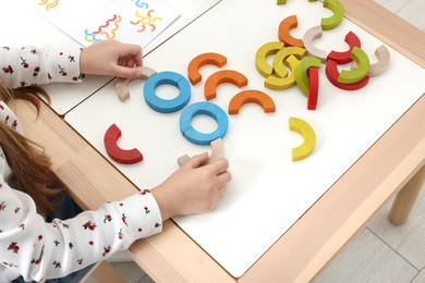 Photo of Motor skills development. Girl playing with colorful wooden arcs at white table indoors, closeup