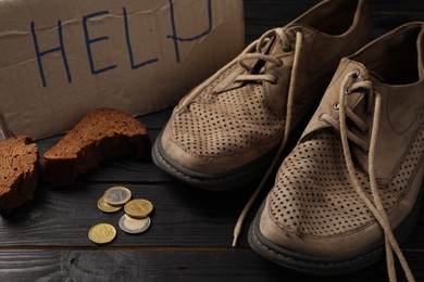 Photo of Poverty. Cardboard sign with word Help, old shoes, pieces of bread and coins on black wooden table
