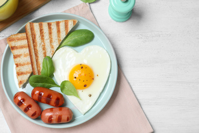 Tasty breakfast with heart shaped fried egg served on white wooden table, flat lay. Space for text