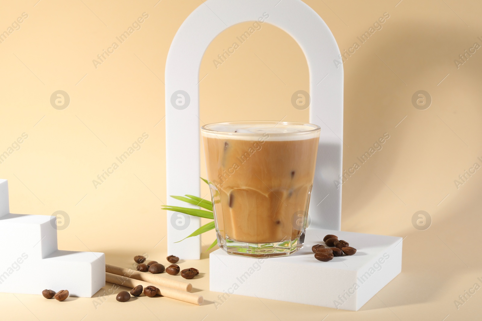 Photo of Refreshing iced coffee with milk in glass and beans on pale yellow background