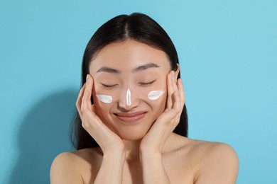 Photo of Beautiful young woman with sun protection cream on her face against light blue background