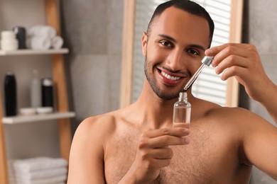 Handsome man with cosmetic serum in hands in bathroom, space for text