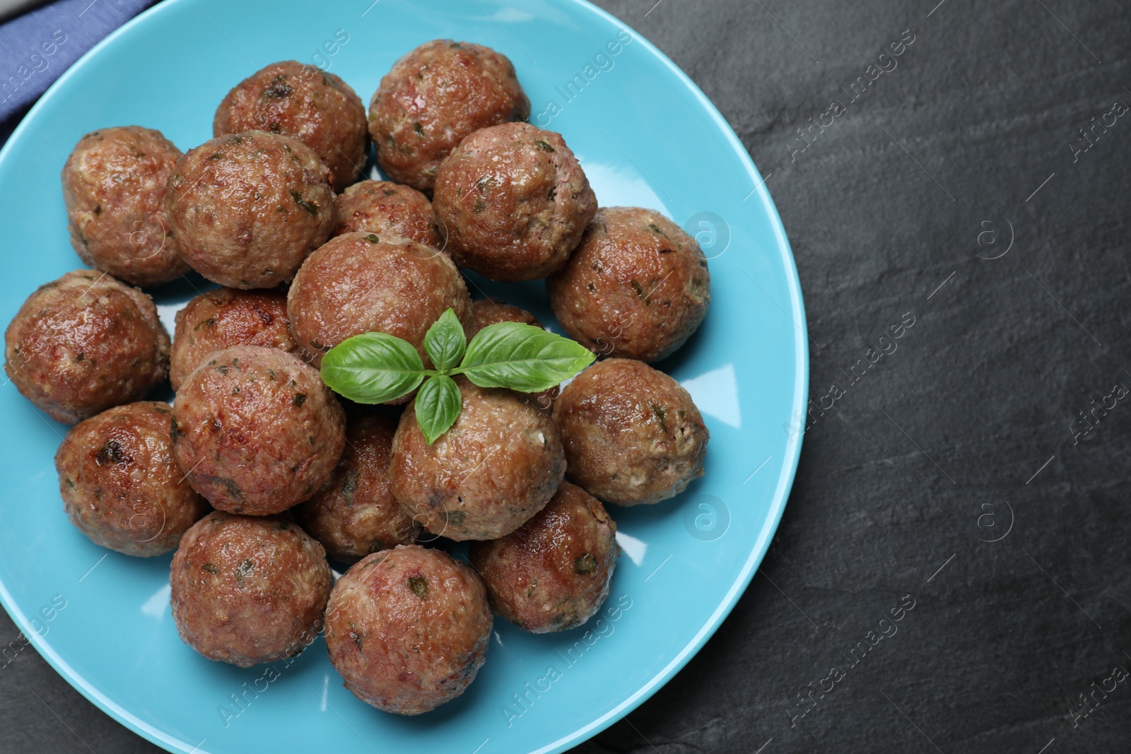 Photo of Tasty cooked meatballs with basil on black table, top view