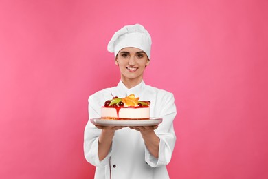 Photo of Happy professional confectioner in uniform holding delicious cake on pink background