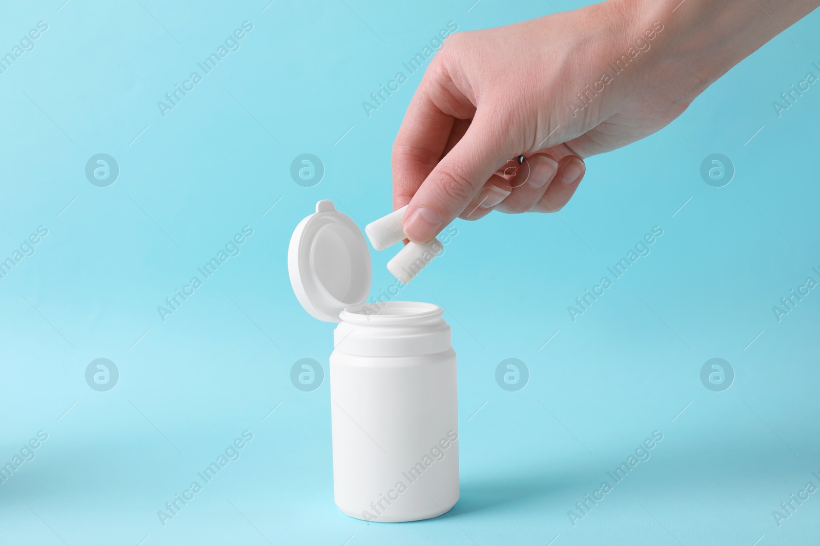 Photo of Woman taking chewing gums from jar on light blue background, closeup