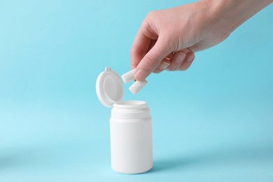 Photo of Woman taking chewing gums from jar on light blue background, closeup