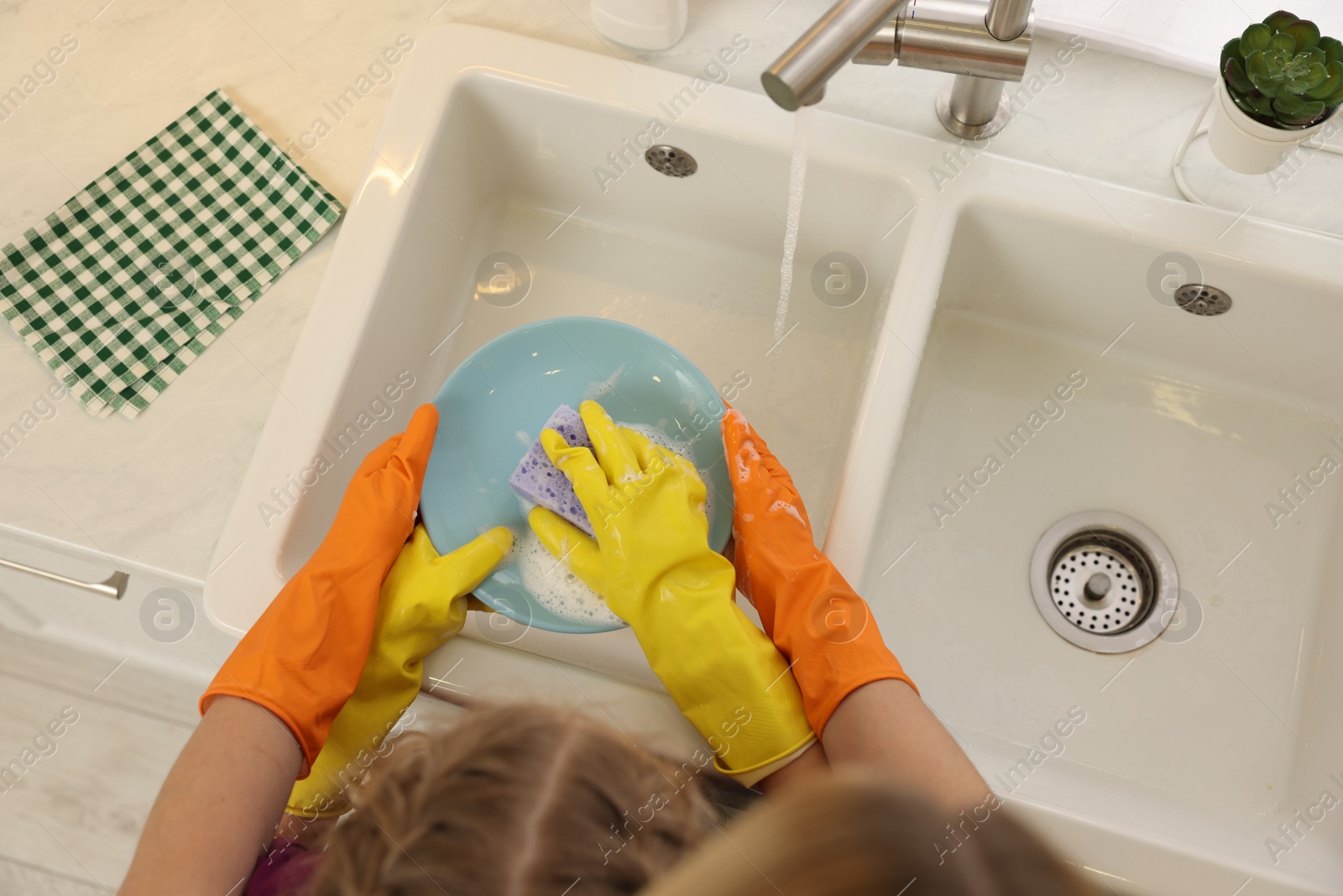 Photo of Mother and daughter in protective gloves washing plate above sink, top view